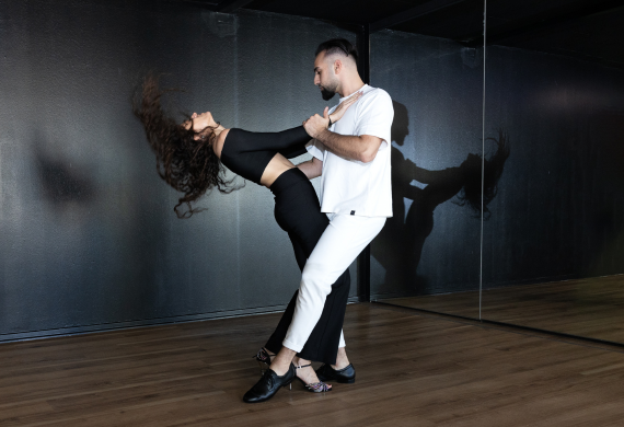Ein Paar tanzt elegant im Innenbereich, wobei eine Spiegelwand ihre Bewegungen reflektiert.