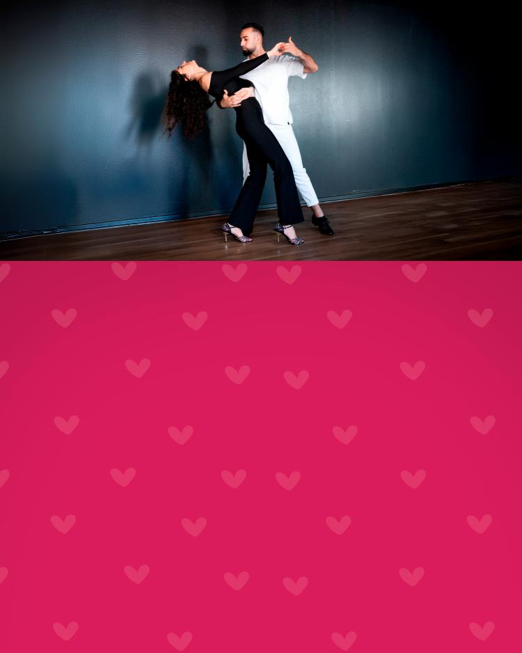 Ein Paar tanzt anmutig in einem Studio vor einer dunklen Wand, darunter ein rosa Rand mit Herzmuster.