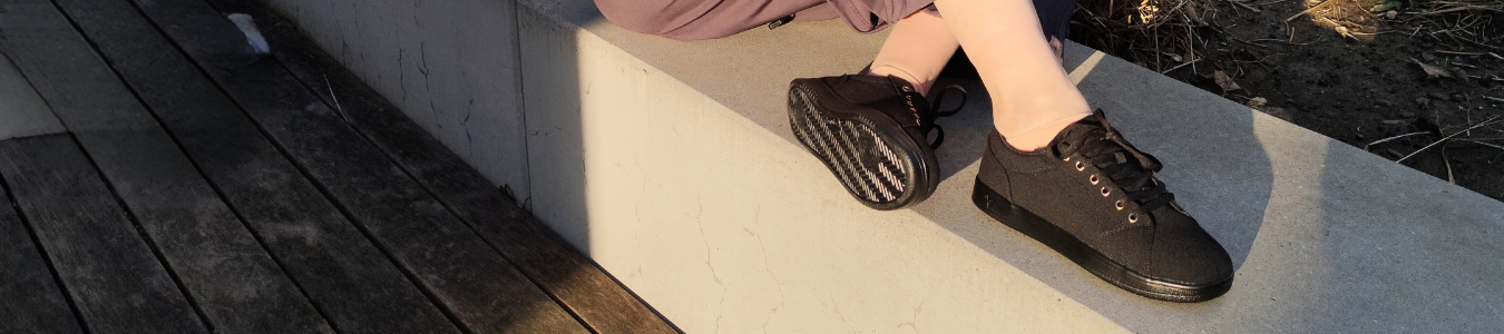 Eine Person sitzt auf einem Betonvorsprung, trägt schwarze Turnschuhe und das Sonnenlicht wirft Schatten.