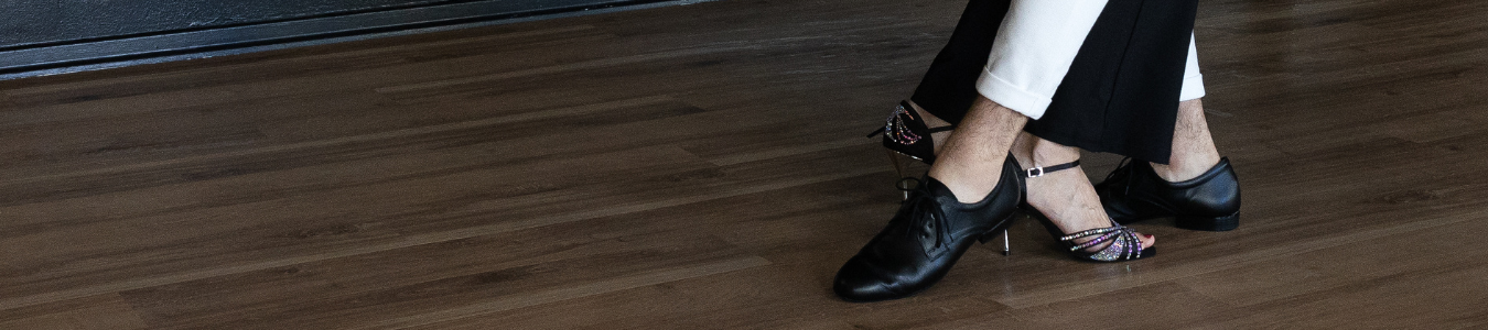 Ein Paar tanzt in schwarzen und weißen Schuhen auf einem Holzboden.