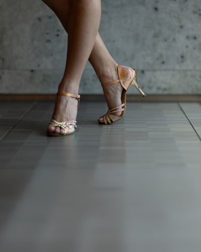 Person in hellbraunen, strassbesetzten Tanzschuhen für den Gesellschaftstanz auf einem gefliesten Boden.