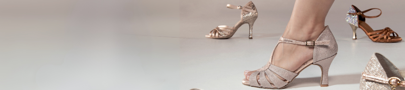 Ein Fuß in einem glitzernden High Heels-Schuh, während andere ähnliche Schuhe verstreut auf einem hellen Boden liegen.