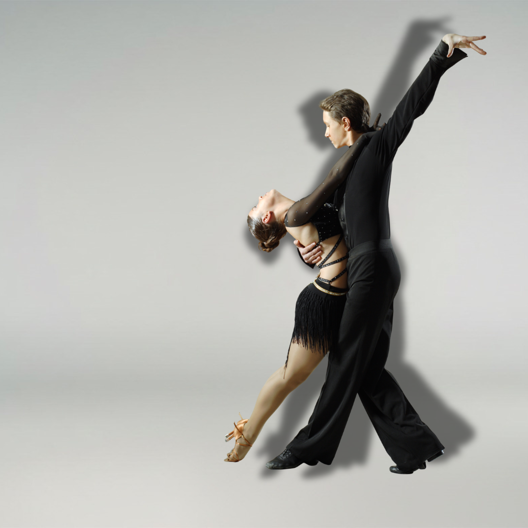 Ein Paar in Gesellschaftstanzkleidung nimmt eine dramatische Pose vor einem schlichten, hellgrauen Hintergrund ein.