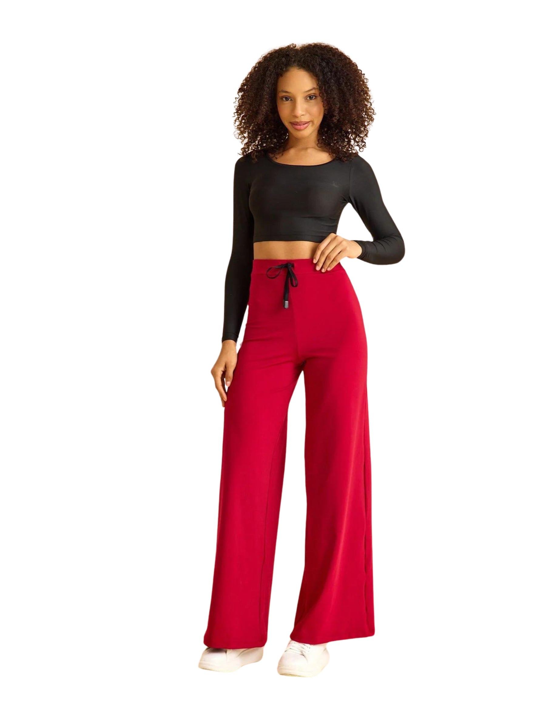 Frau in schwarzem Crop-Top und Lisminas 448 Mumbai Yoga Hose in Bordeaux posiert selbstbewusst vor weißem Hintergrund.