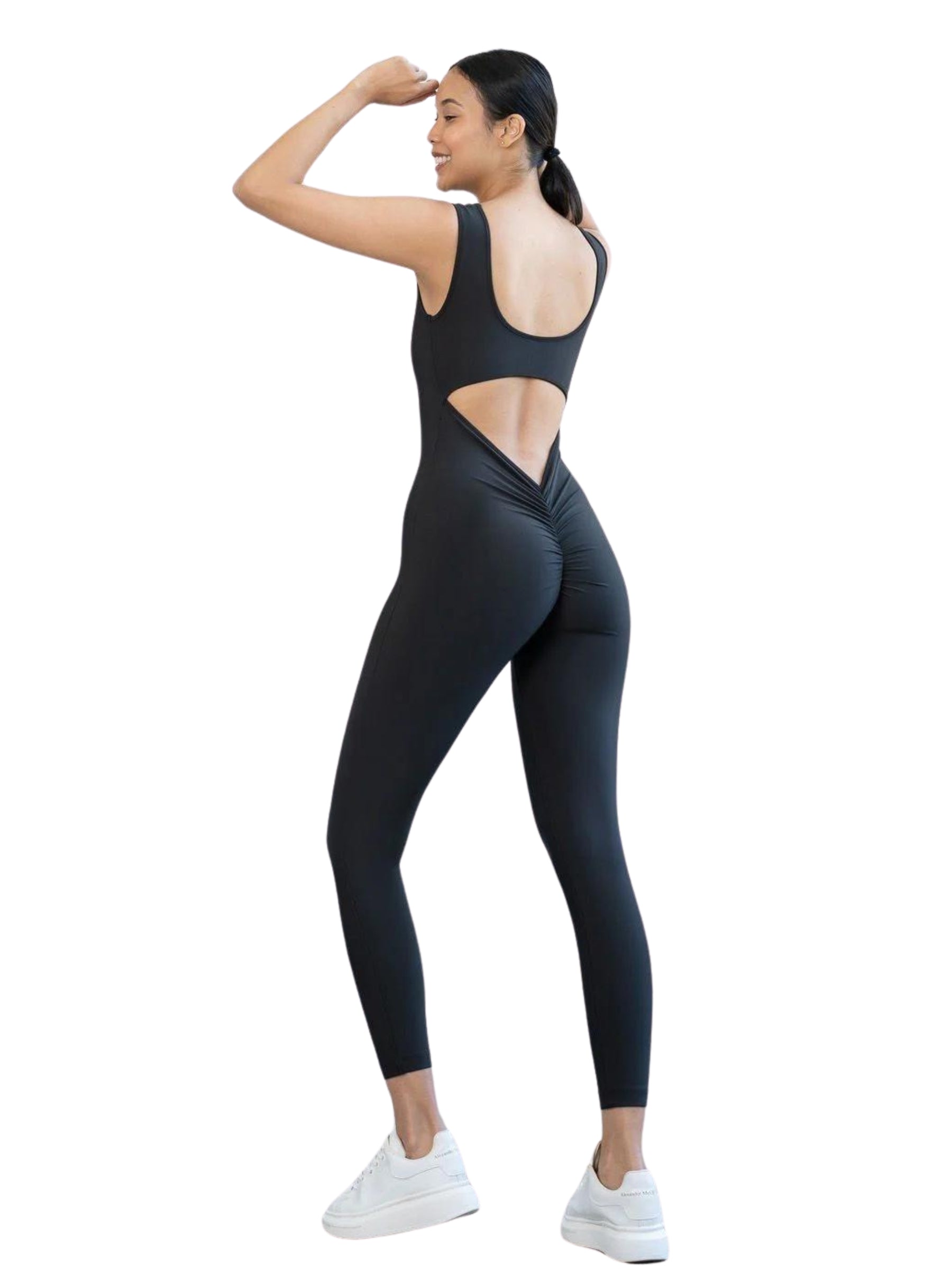 Frau im 1400 Scrunch Butt Jumpsuit in Schwarz von Lismina, weiße Turnschuhe, erhobener Arm.