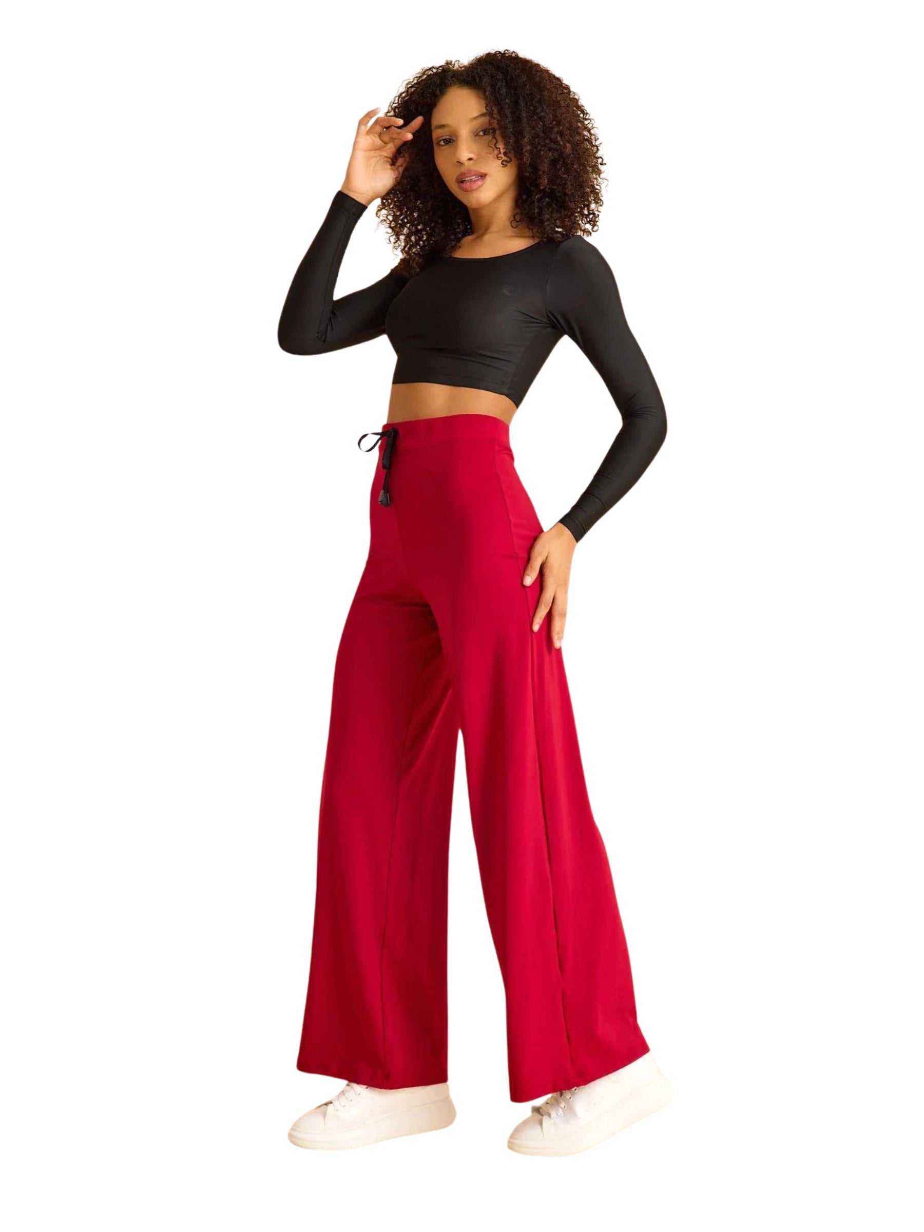 Frau in schwarzem bauchfreiem Top und Lisminas 448 Mumbai Yoga Hose posiert vor einem weißen Hintergrund und trägt weiße Turnschuhe.