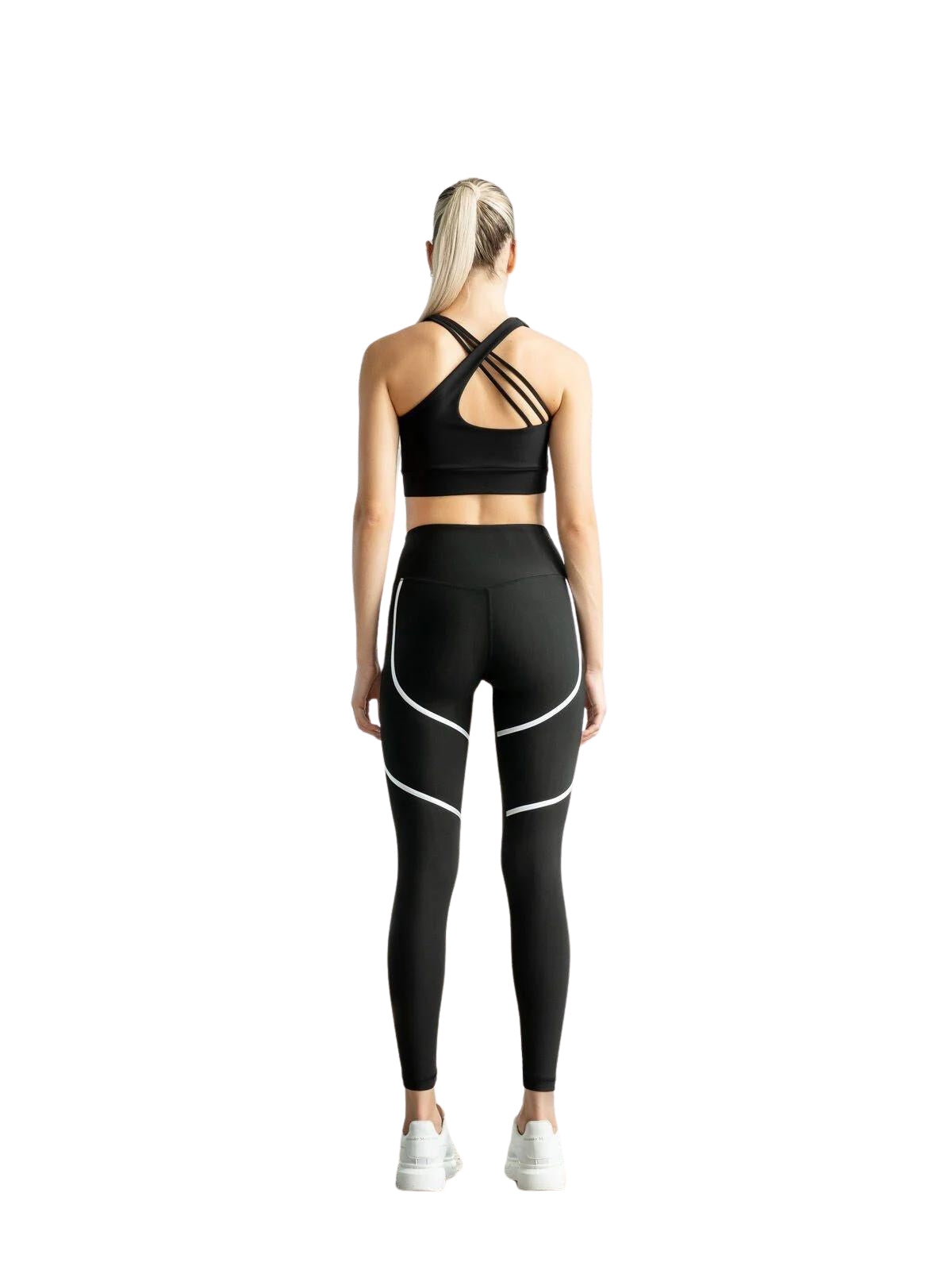 Blondes Mädchen mit Pferdeschwanz, das Lisminas 394 Orly Sport Leggings in Schwarz & Weiß trägt, steht mit dem Gesicht abgewandt vor einem weißen Hintergrund.