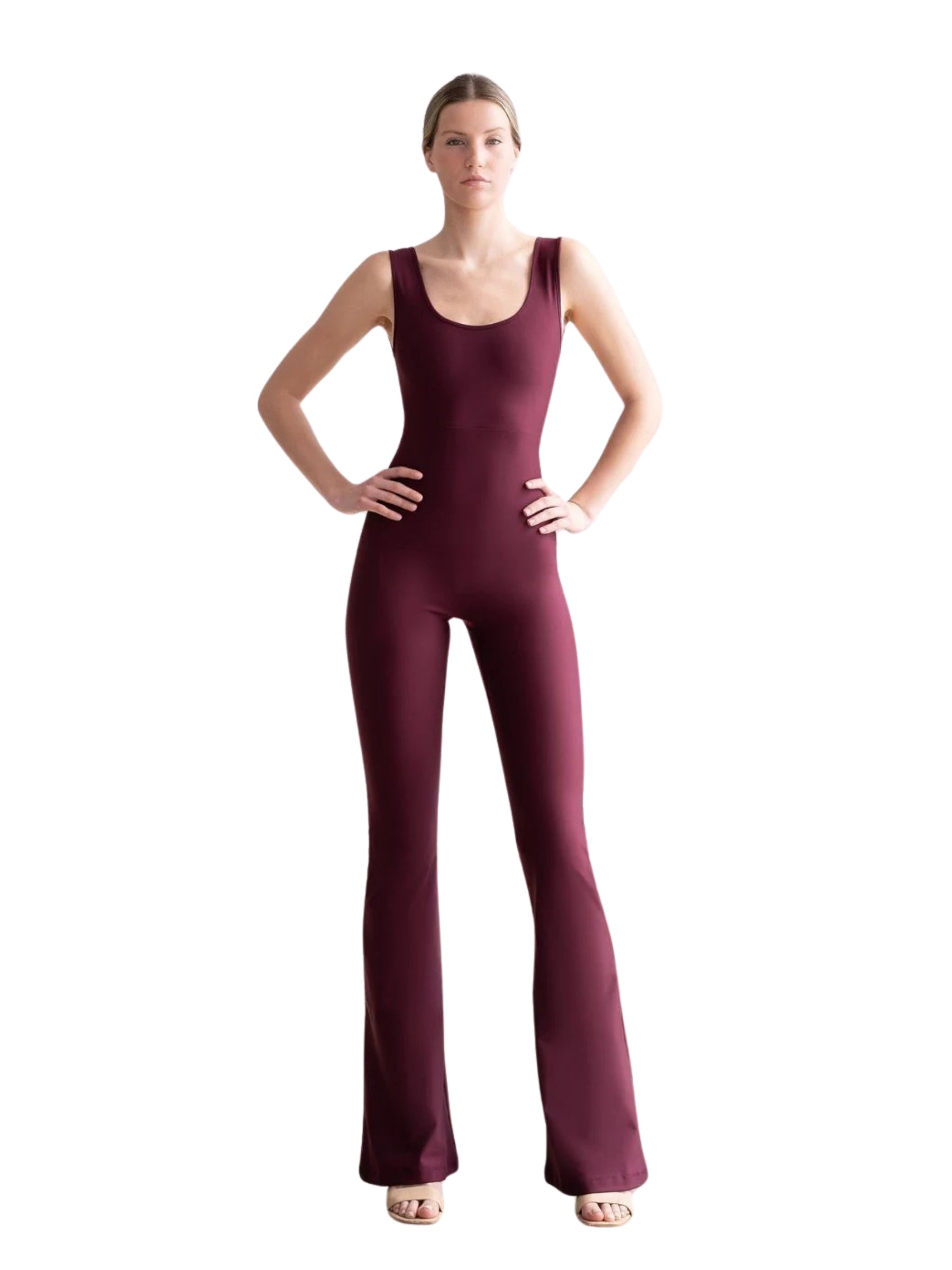 Das Model im 1501 Spanish Scrunch Butt Jumpsuit von Lismina, Dunkelviolett, posiert mit den Händen in den Hüften vor einem weißen Hintergrund.