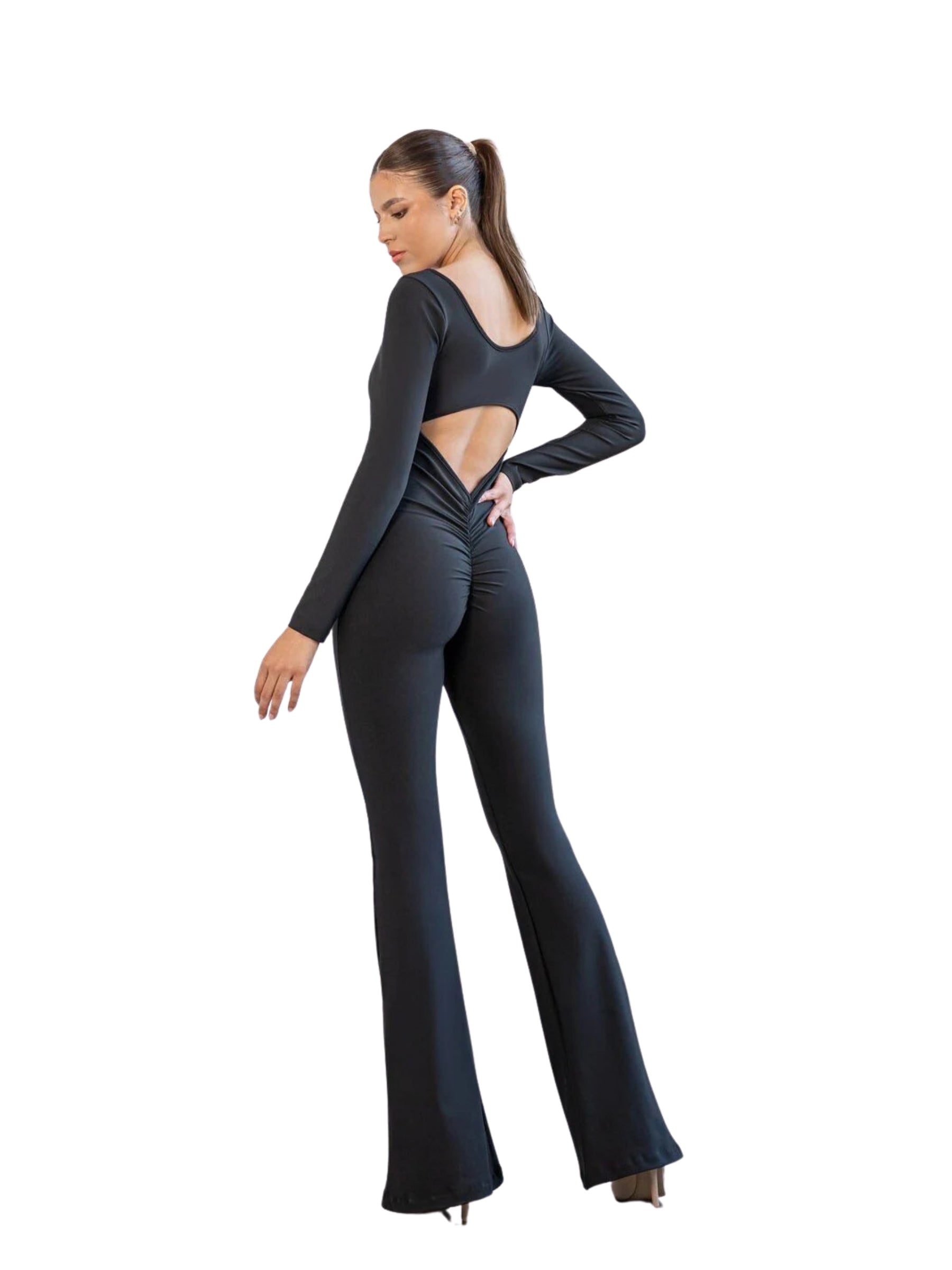 Frau trägt Lismina 3100 Spanish Scrunch Butt Jumpsuit in Schwarz, stehend und über ihre Schulter blickend.