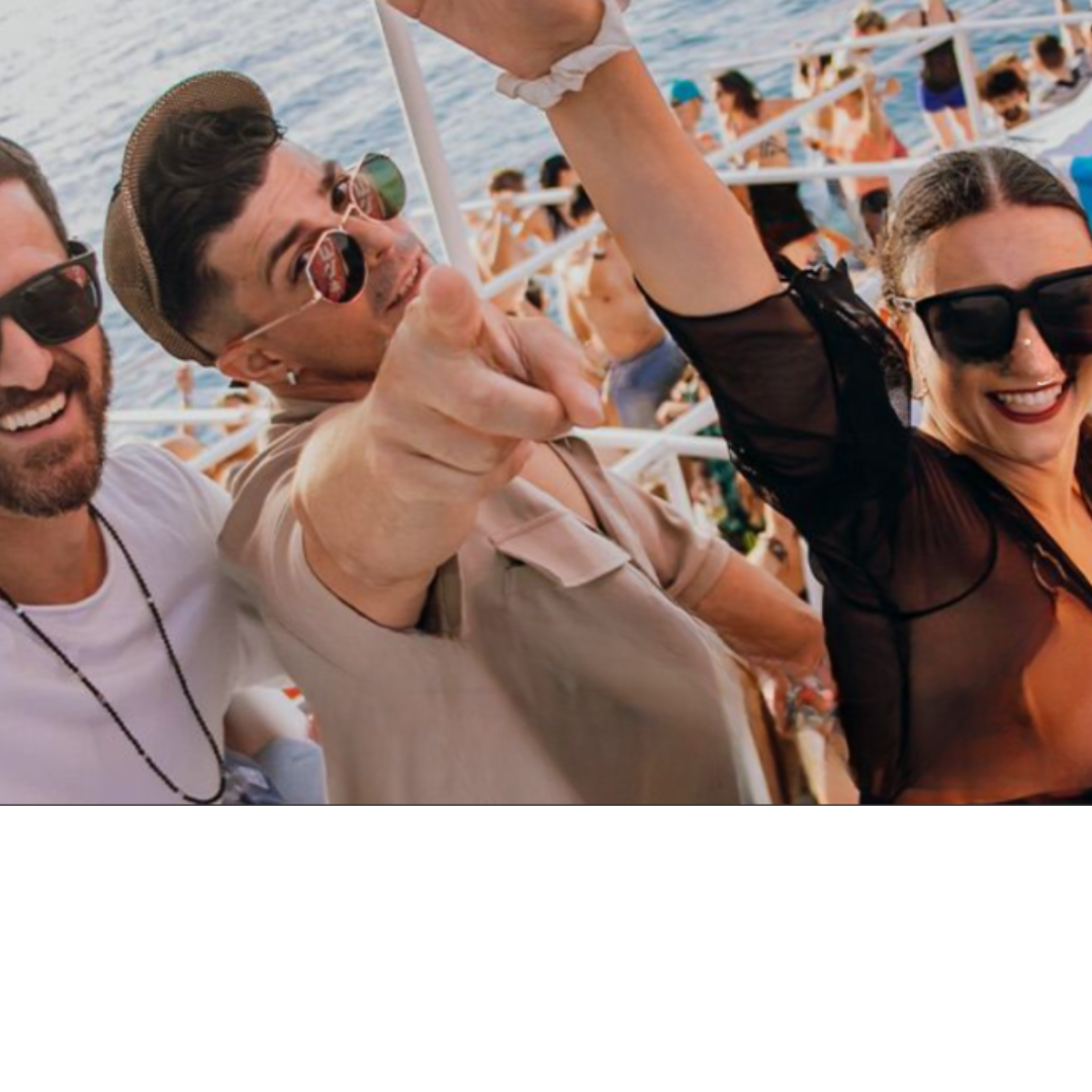 Drei Freunde mit Sonnenbrillen lächeln und machen ein Selfie auf einer lebhaften Party im Freien am Wasser.