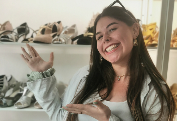 Lächelnde Frau deutet auf Schuhauslagen in Regalen.