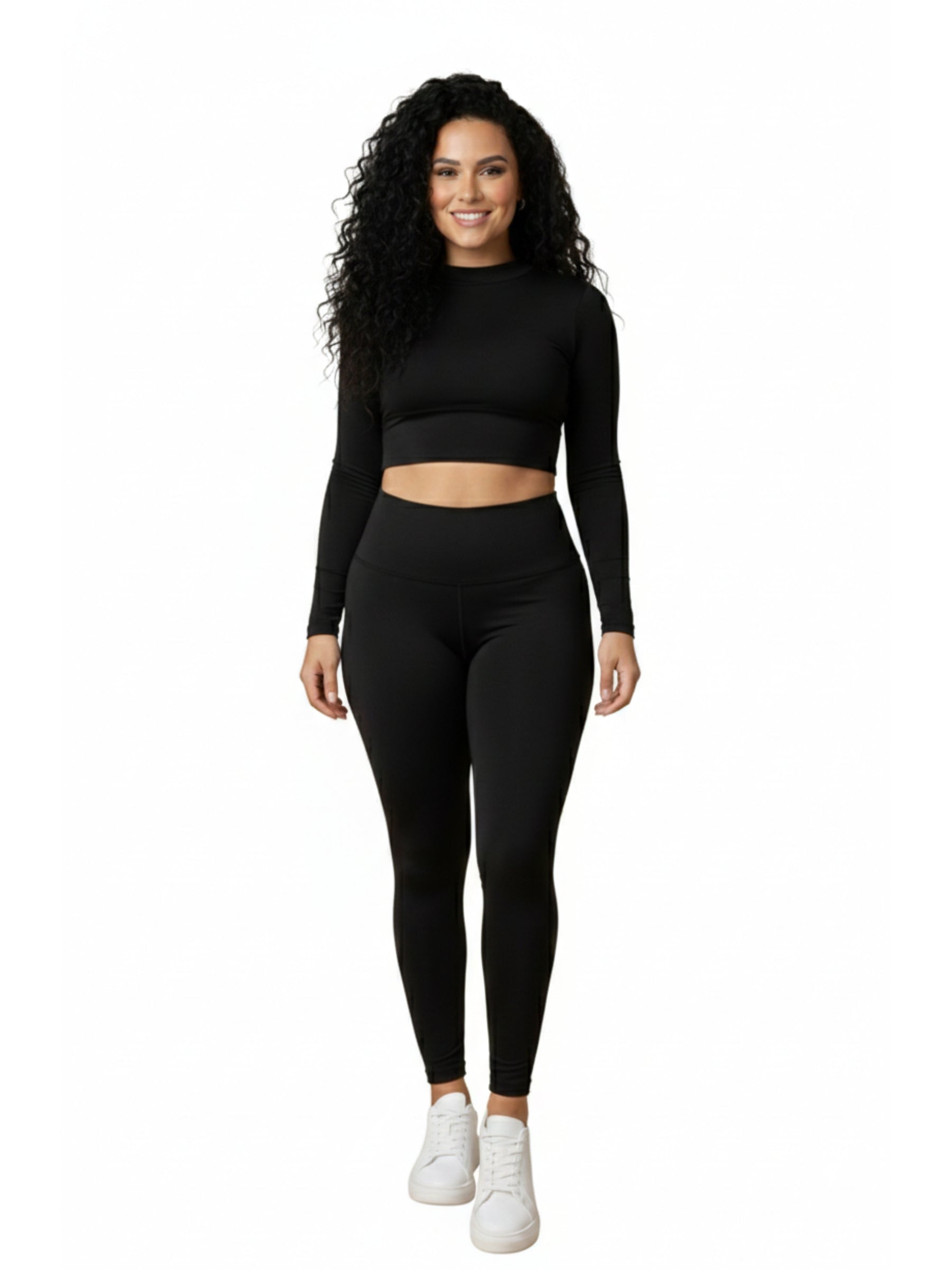 Lächelnde Frau mit lockigem Haar in Dancing Queens Pulse High Waist Leggings in Schwarz und Crop Top, weiße Sneakers.