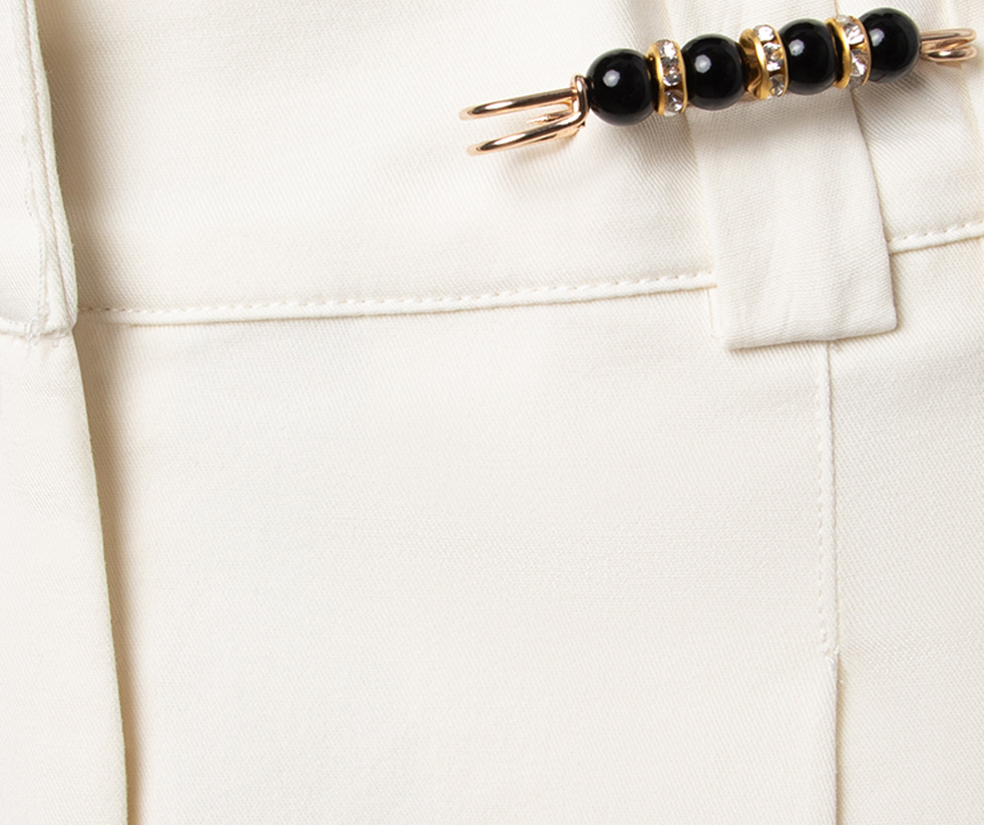 Nahaufnahme der cremefarbenen Hose mit Dancing Queens Sicherheitsnadeln mit Perlen im Set, ideal für Bühnenauftritte.