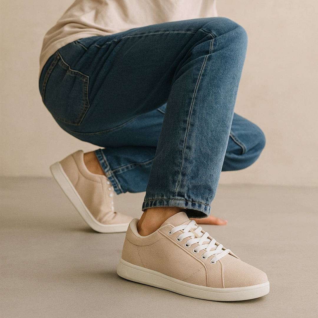 Hockende Person in blauen Jeans und beigen Turnschuhen vor einem neutralen Hintergrund.