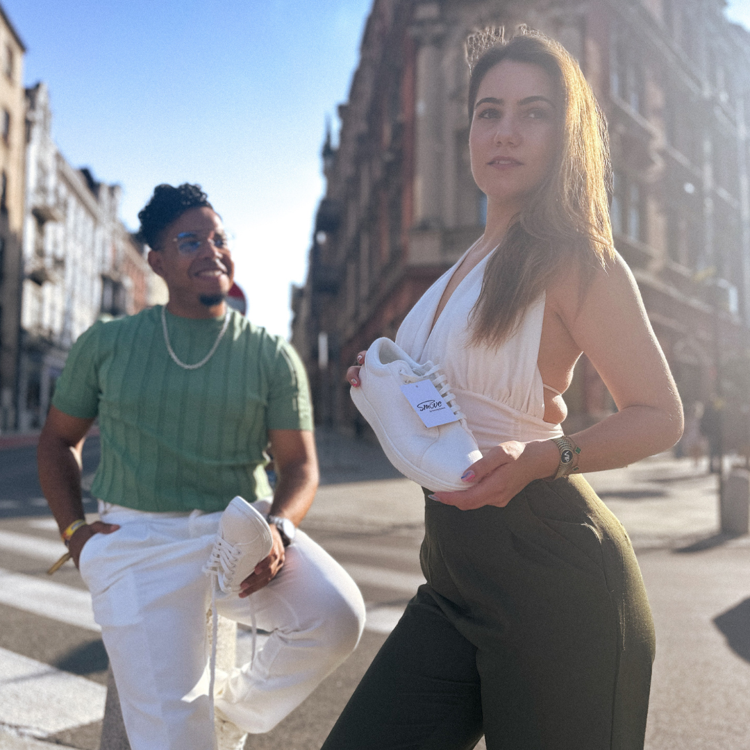 Zwei Personen posieren im Freien in weißen Turnschuhen auf einer sonnigen Stadtstraße.