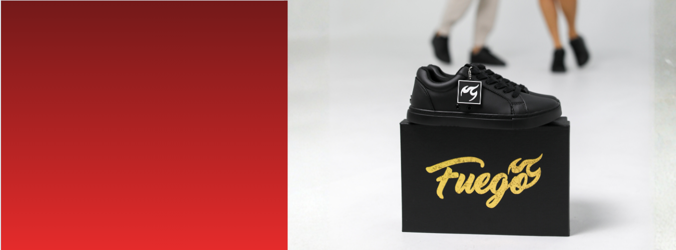 Ein schwarzer Turnschuh auf einem Fuego-Schuhkarton; zwei Personen in Tanzschuhen sind unscharf im Hintergrund zu sehen.