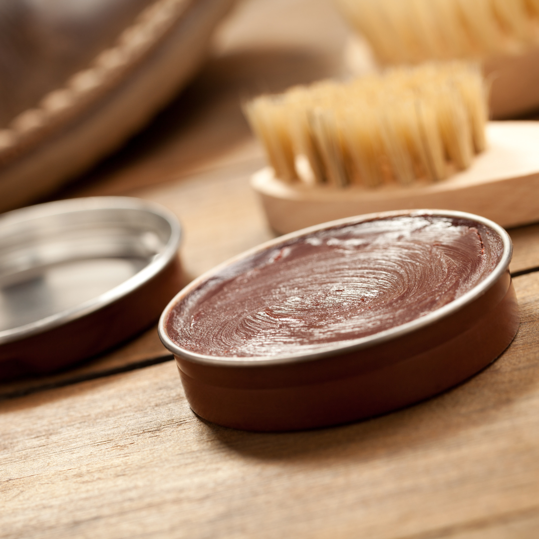 Dose mit brauner Schuhcreme mit einer Schuhbürste auf einer Holzunterlage öffnen.