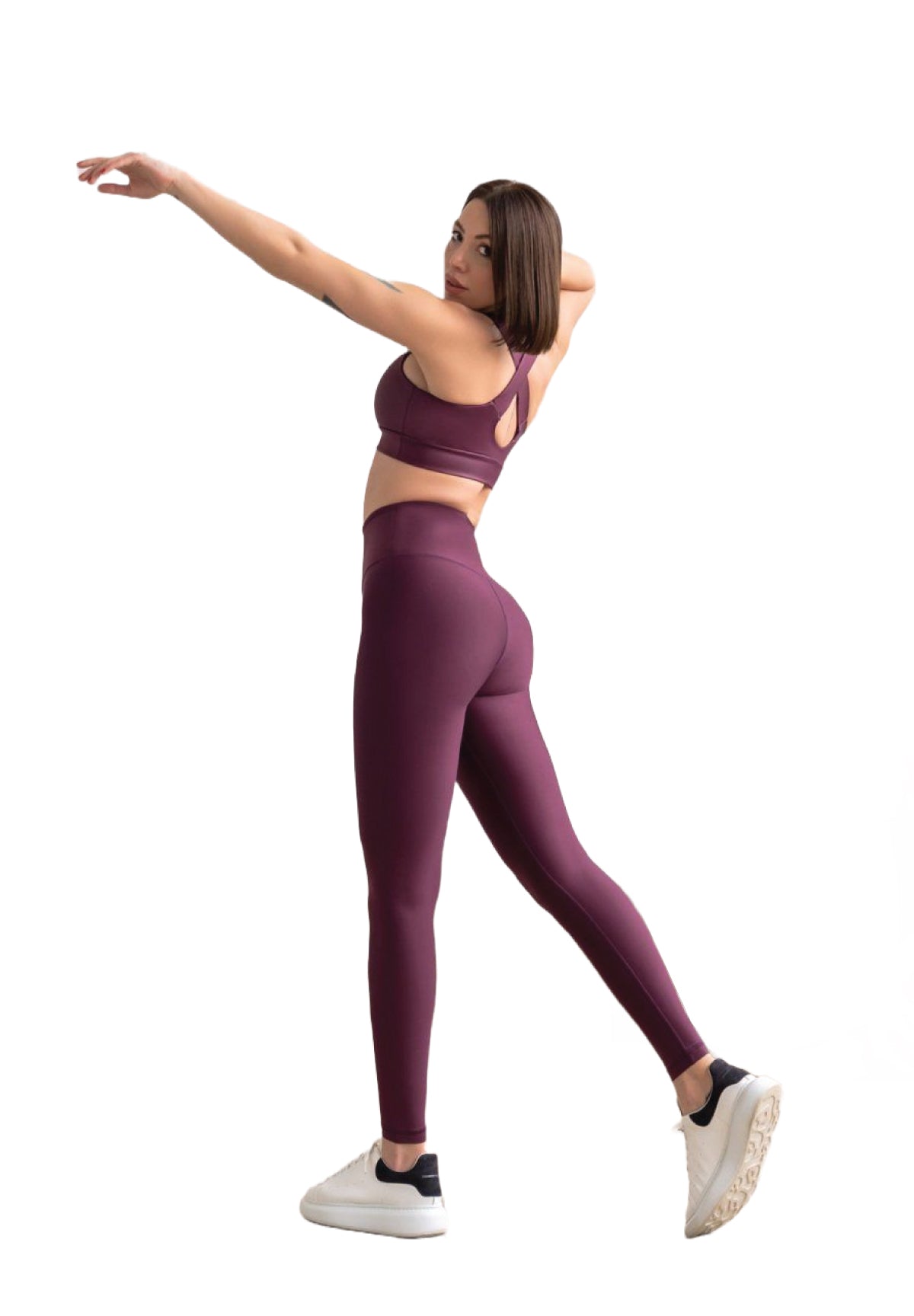 Eine Frau in Lisminas 255 High Waist Leggings in Dunkelviolett streckt sich mit erhobenem Arm und trägt weiße Turnschuhe.