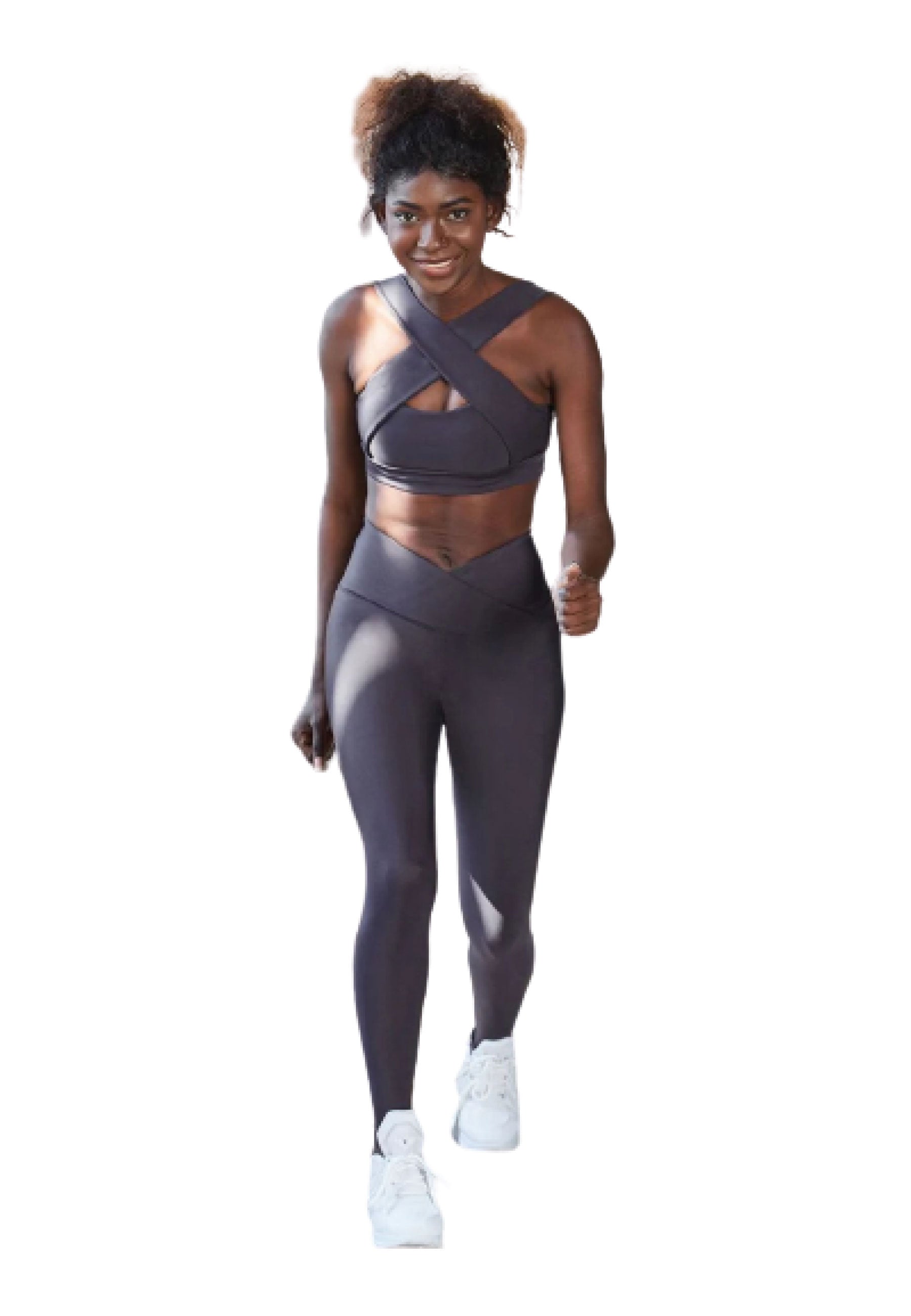 Die Person läuft selbstbewusst in Lisminas 206 Decoltée Sport-BH, schwarzer Criss-Cross-Sportkleidung und weißen Turnschuhen und lächelt.