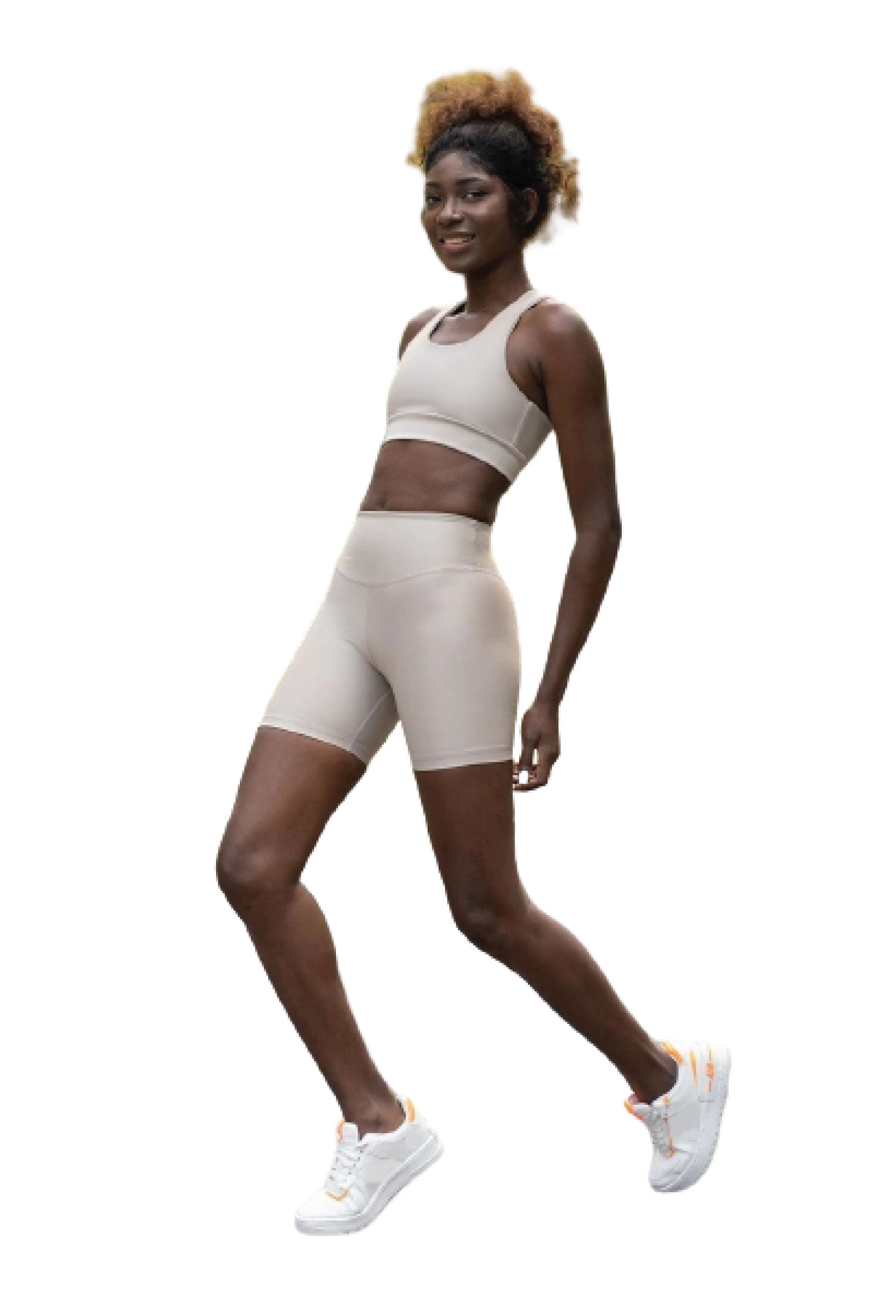 Die Person in Lisminas 209 Single Crossed Sport Bra in Beige und weißen Sneakers steht selbstbewusst auf einem Bein und lächelt.