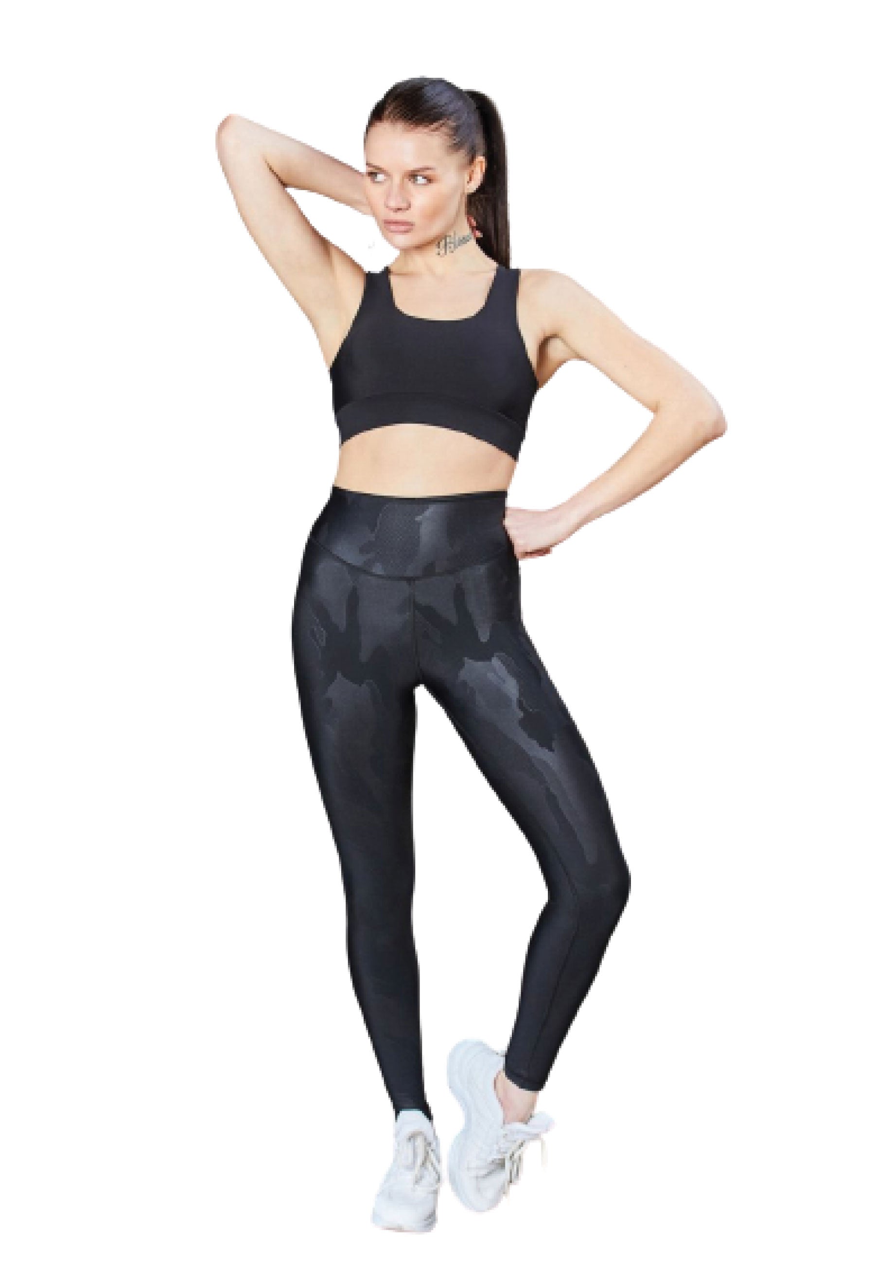 Person in Lismina 1058 Schwarz-Lederleggings, Sport-BH und weißen Turnschuhen, posiert mit der Hand auf der Hüfte und erhobenem Arm.