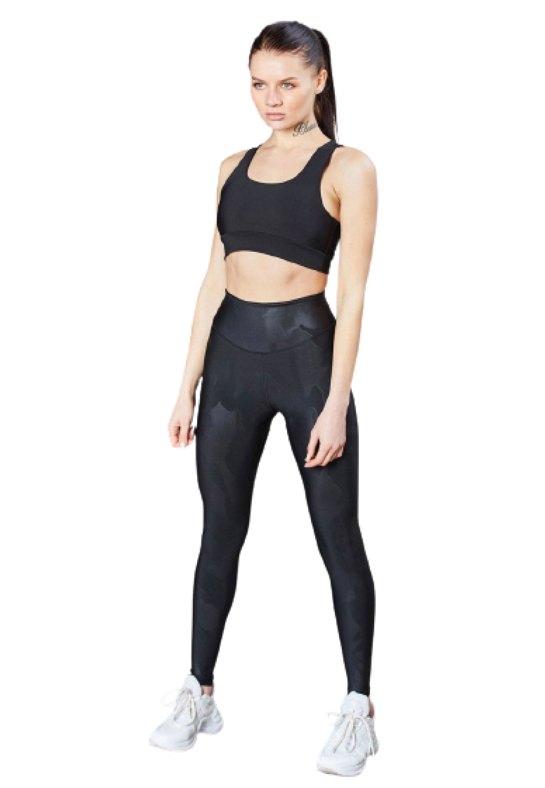 Person in Lisminas 1058 Leder-Look-Leggings in Schwarz, schwarzem Sport-BH und weißen Turnschuhen, steht mit ausgestreckten Armen da.