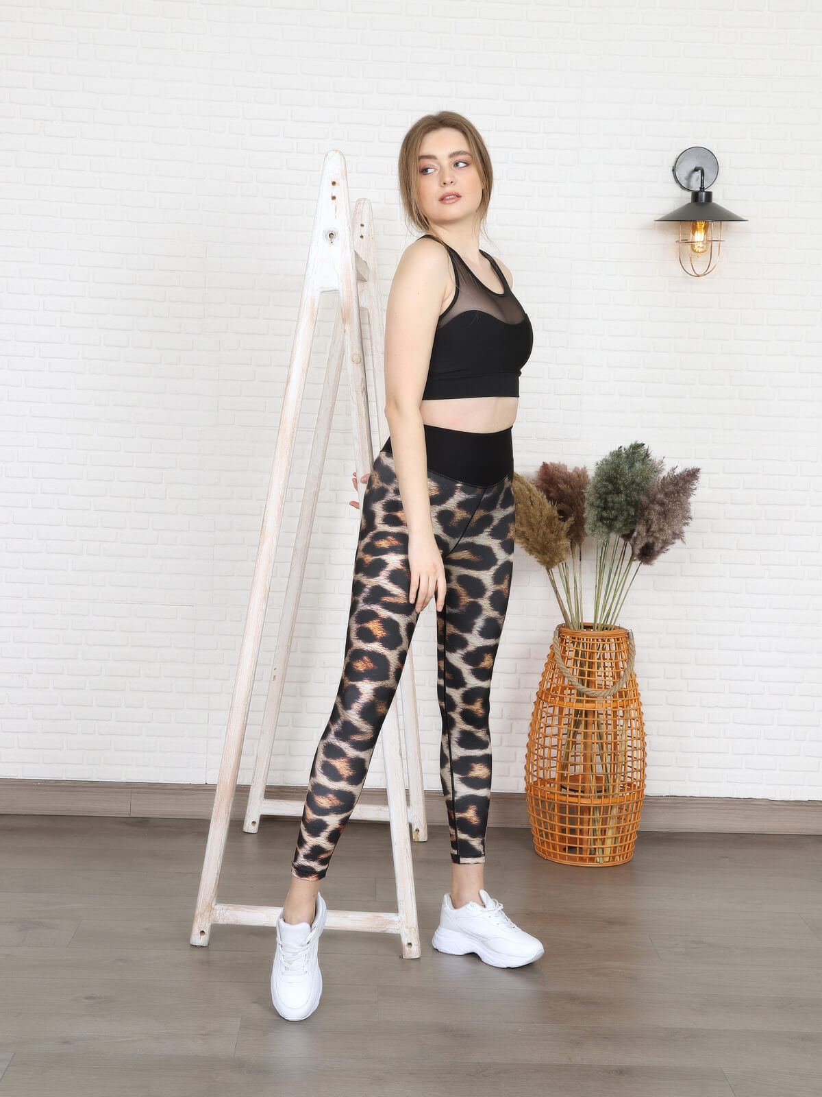Eine Person in einem schwarzen Oberteil und Lisminas 1080 Extra High Waist Leopard Leggings steht neben einer Holzleiter, in der Nähe Pampasgras.