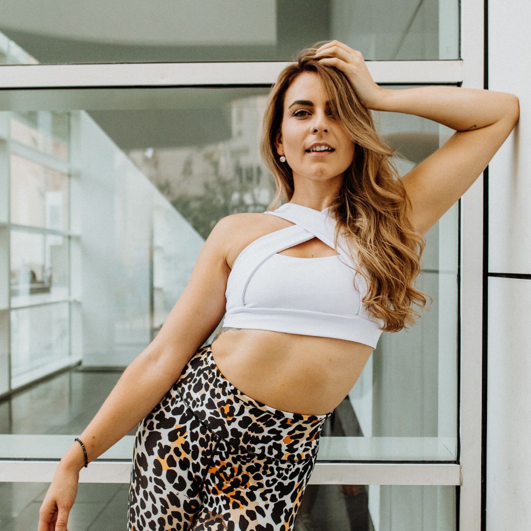 Andrea Gabriela posiert selbstbewusst in Fitnesskleidung : weißes Top, Leggings mit Leopardenmuster.