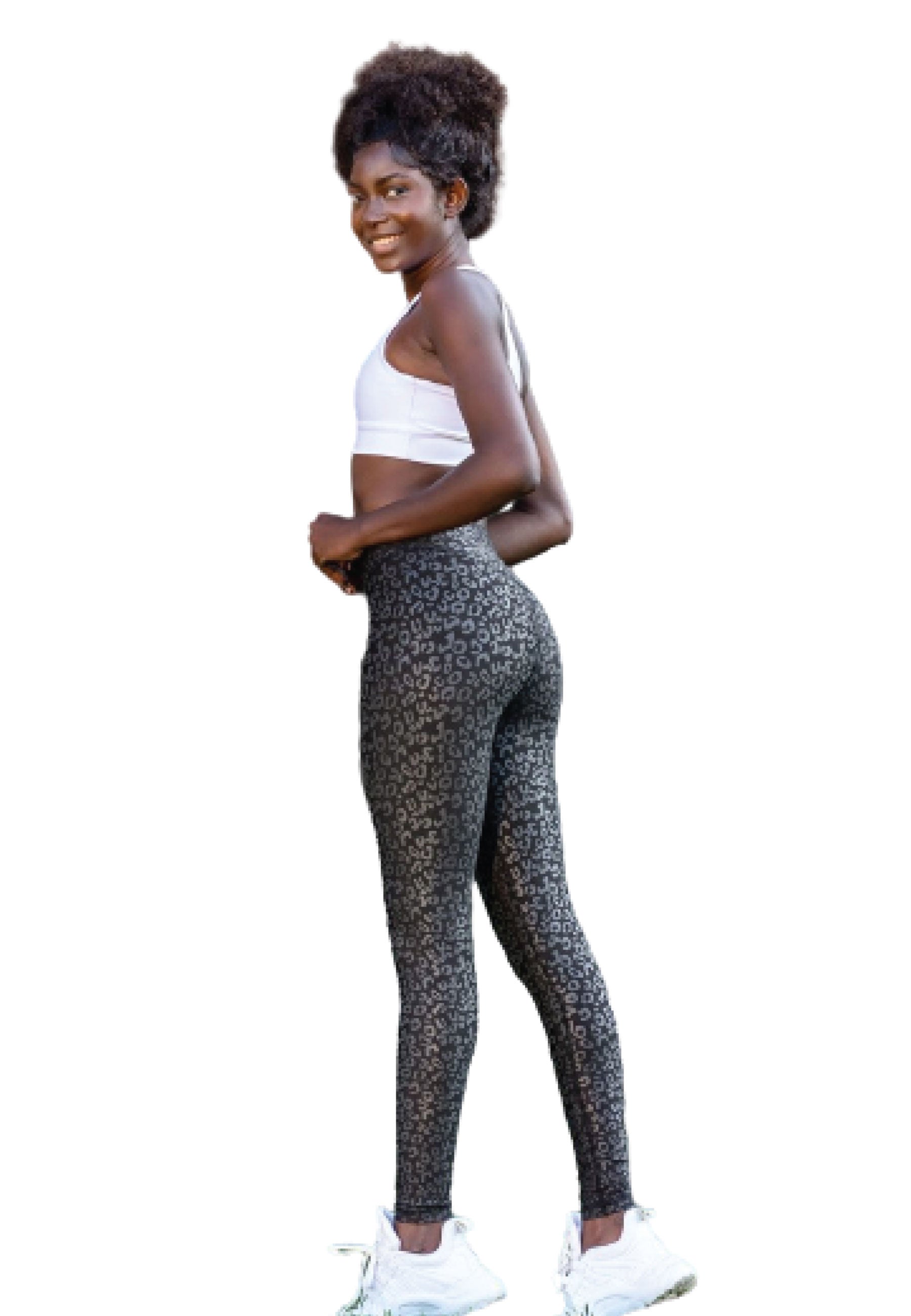 Frau in Lismina 1150-Leggings in Lederoptik, weißem Sport-BH und Turnschuhen, lächelt vor weißem Hintergrund.